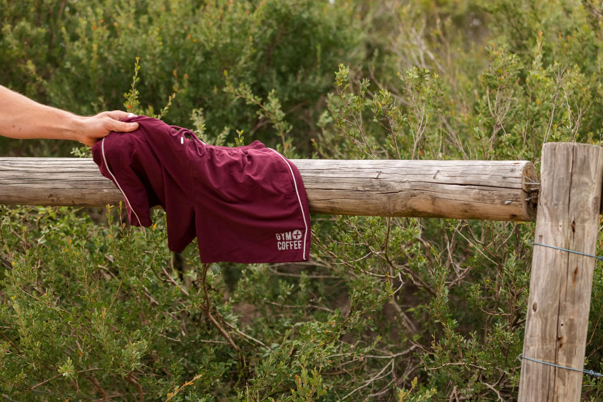gym-coffee-rpet-swim-shorts Gym+Coffee swim shorts made from recycled polyester, hanging on a wooden fence