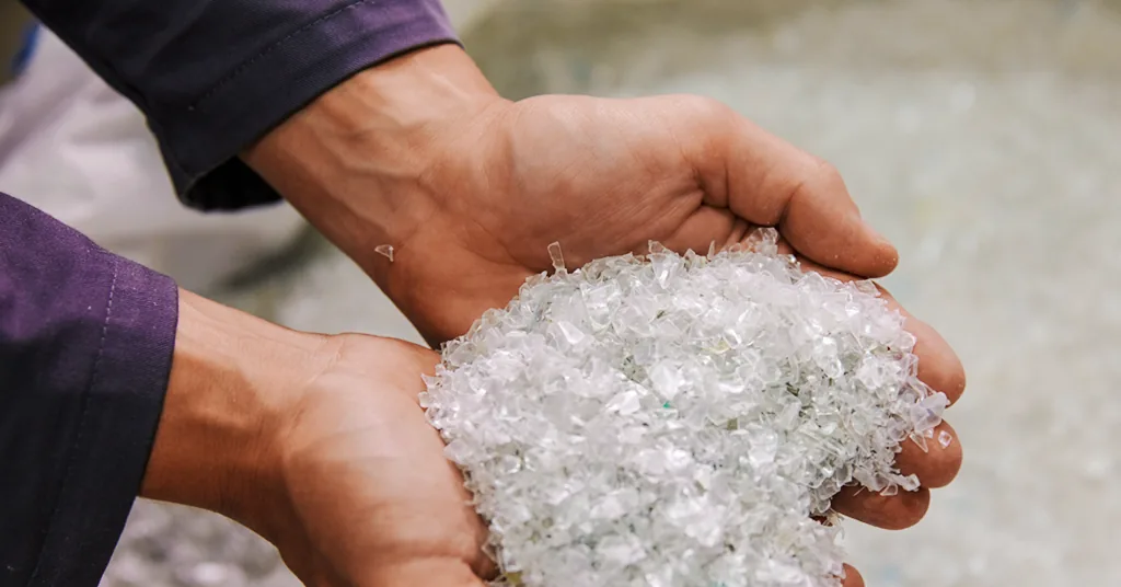 Hands holding clean, clear PET bottle flakes ready to be melted and spun into rPET yarn